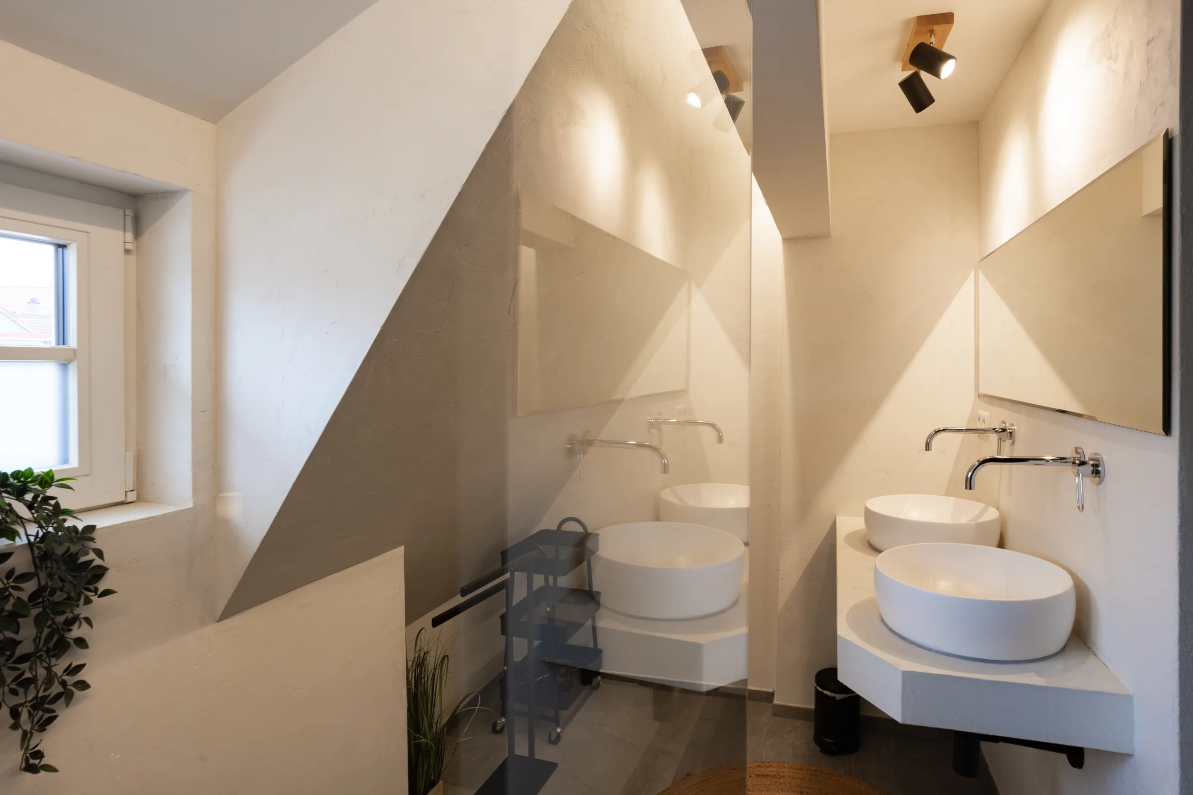 Kleines Bad mit zwei runden Aufsatzbecken, wandmontierten Armaturen, großem Spiegel und sichtbarer Dachschräge